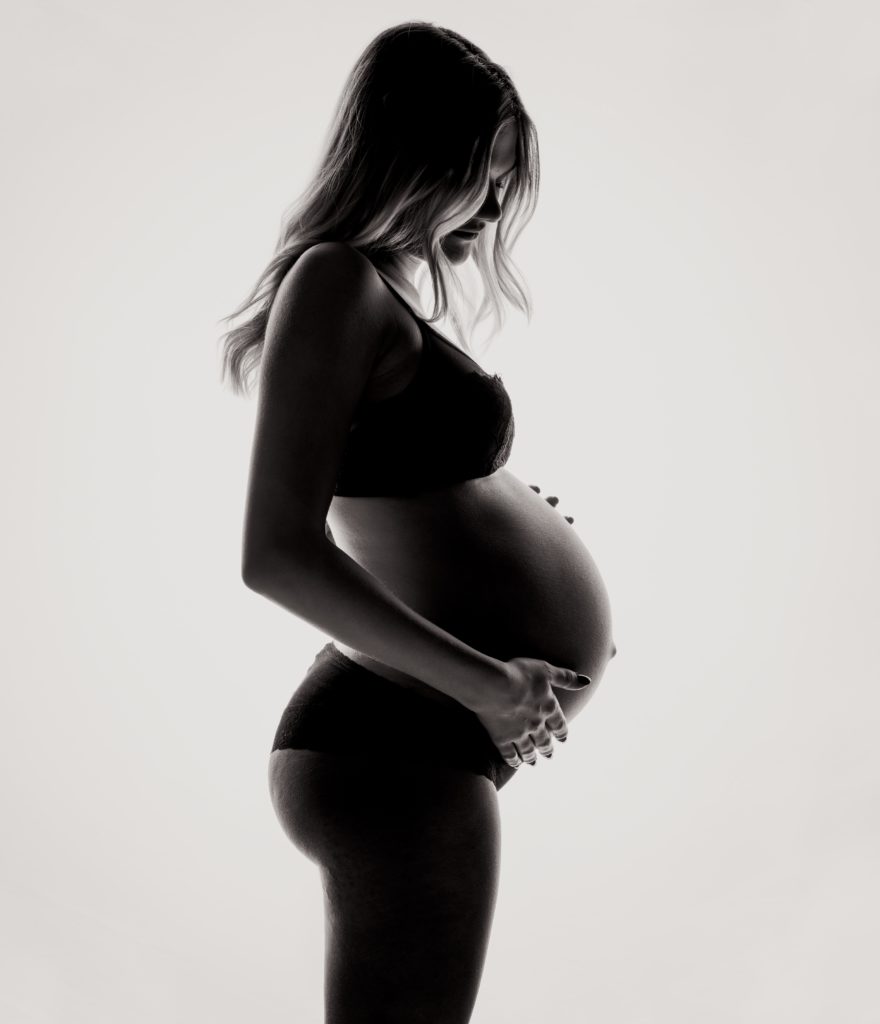 A pregnant woman silhouette stands holding her belly