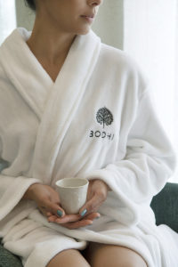 Closeup image of woman wearing BODHI robe, sitting with teacup in hands